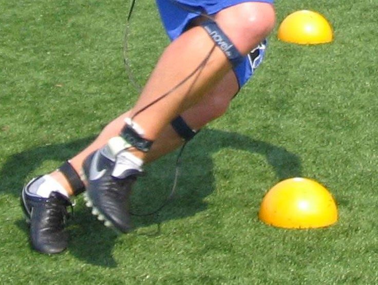 The knee down of a person fitted with the pedar equipment while completing a cutting task around yellow cones wearing cleats.