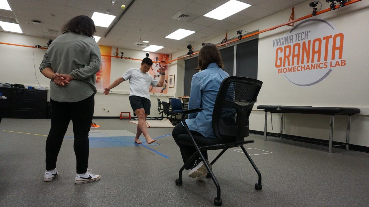 Image of a research participant performing a balance exercise while standing on a force plate and two researchers look on.